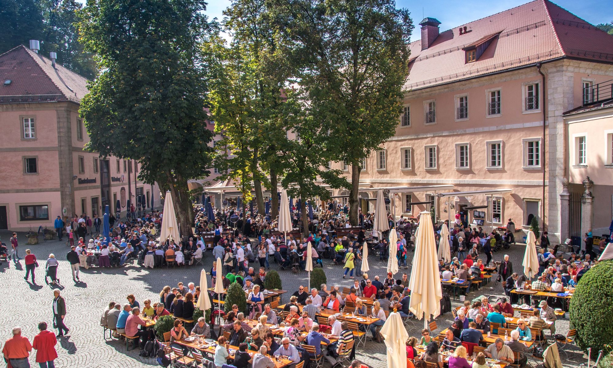 The packed beer garden courtyard of the Klosterschenke Weltenburg monastery tavern in Kelheim, with hundreds of drinkers at long tables.