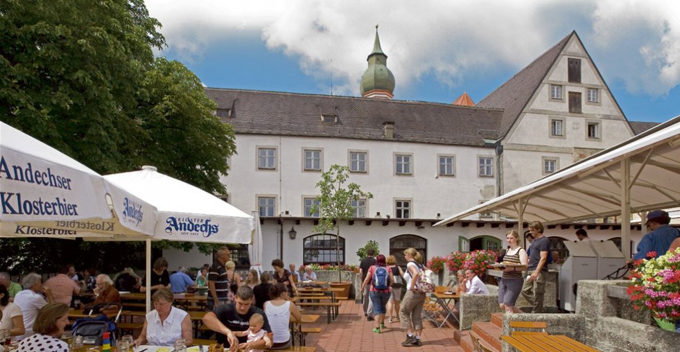 Guests at the beer garden tables in front of the Kloster Andechs monastery, with Andechser Klosterbier umbrellas.