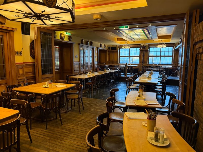The wood-paneled dining hall of Brauhaus Früh am Dom in Cologne with tables set for Kölsch service.