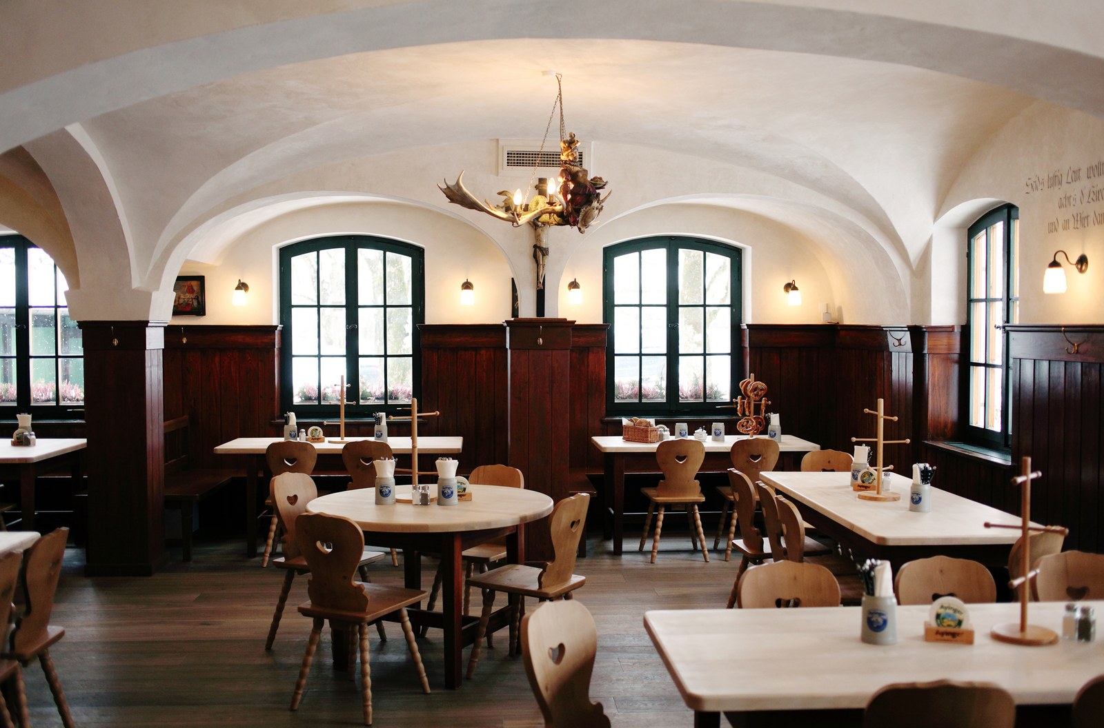 The vaulted interior of the Ayinger Bräustüberl in Aying with antler chandelier and wooden tables set with Ayinger steins.