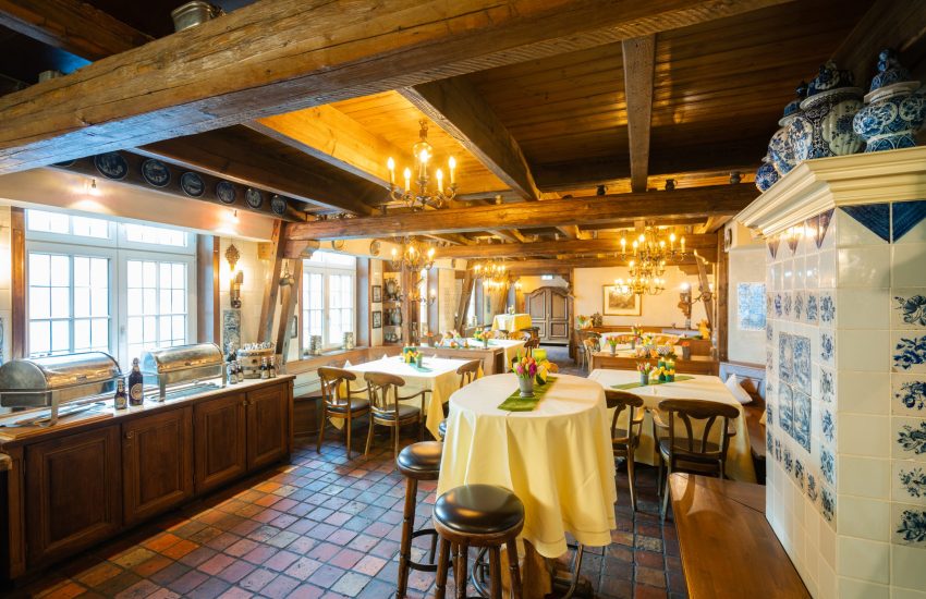 The Braumeisterstube dining room at Brauerei Schumacher in Düsseldorf, with wooden beams, white-tablecloth tables, and a decorated tiled stove.