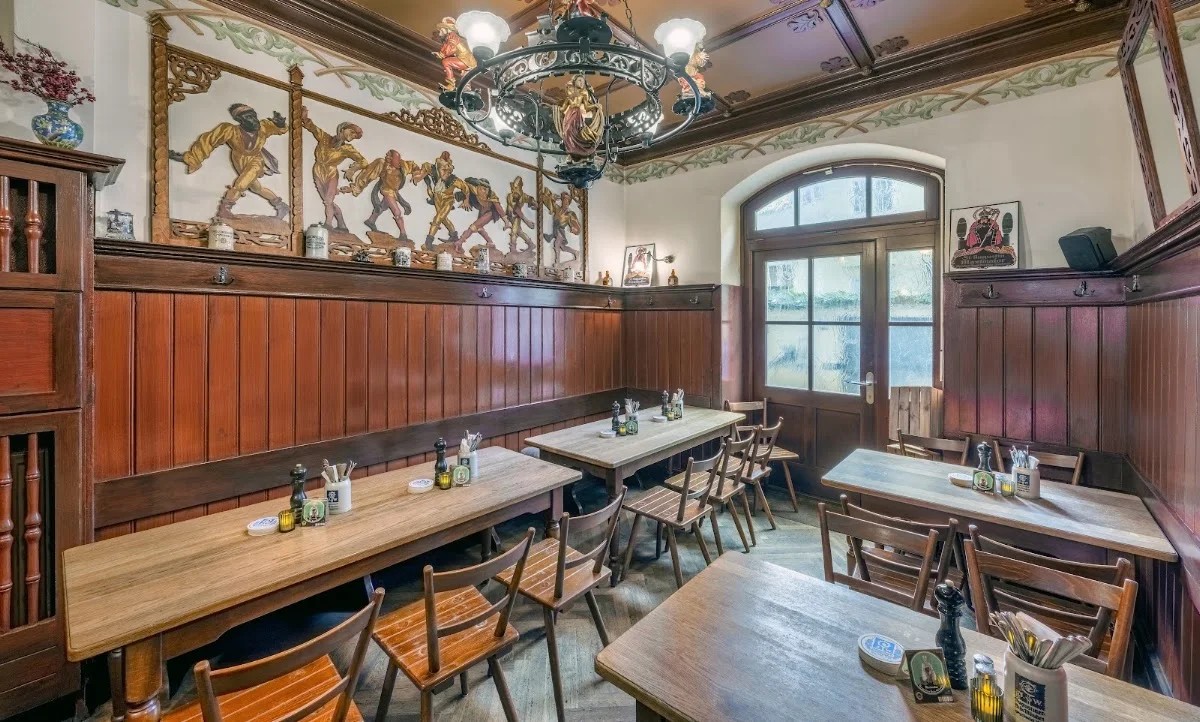 The frescoed vaulted dining hall at Tattenbach Wirtshaus & Stüberl in Munich, with dark wood paneling, long communal tables, and an iron chandelier.