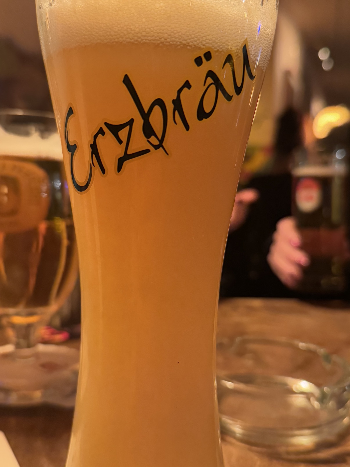 A close-up of a tall Erzbräu Weizen glass with a thick, creamy head — the banana Weisse.
