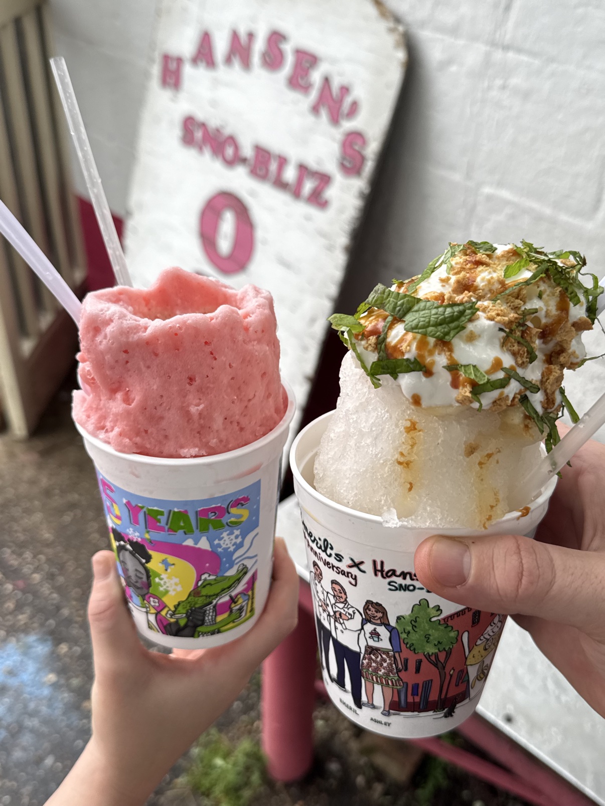 The Hansen's Sno-Bliz stand in Uptown New Orleans with its hand-painted signage, a bright pink shaved-ice snowball with a paper umbrella held up in front of the shop.