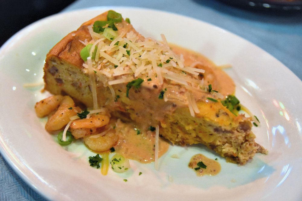 A heaping plate of golden fried shrimp over creamy grits at Jacques-Imo's Cafe in New Orleans, garnished with scallions on a floral-patterned plate.