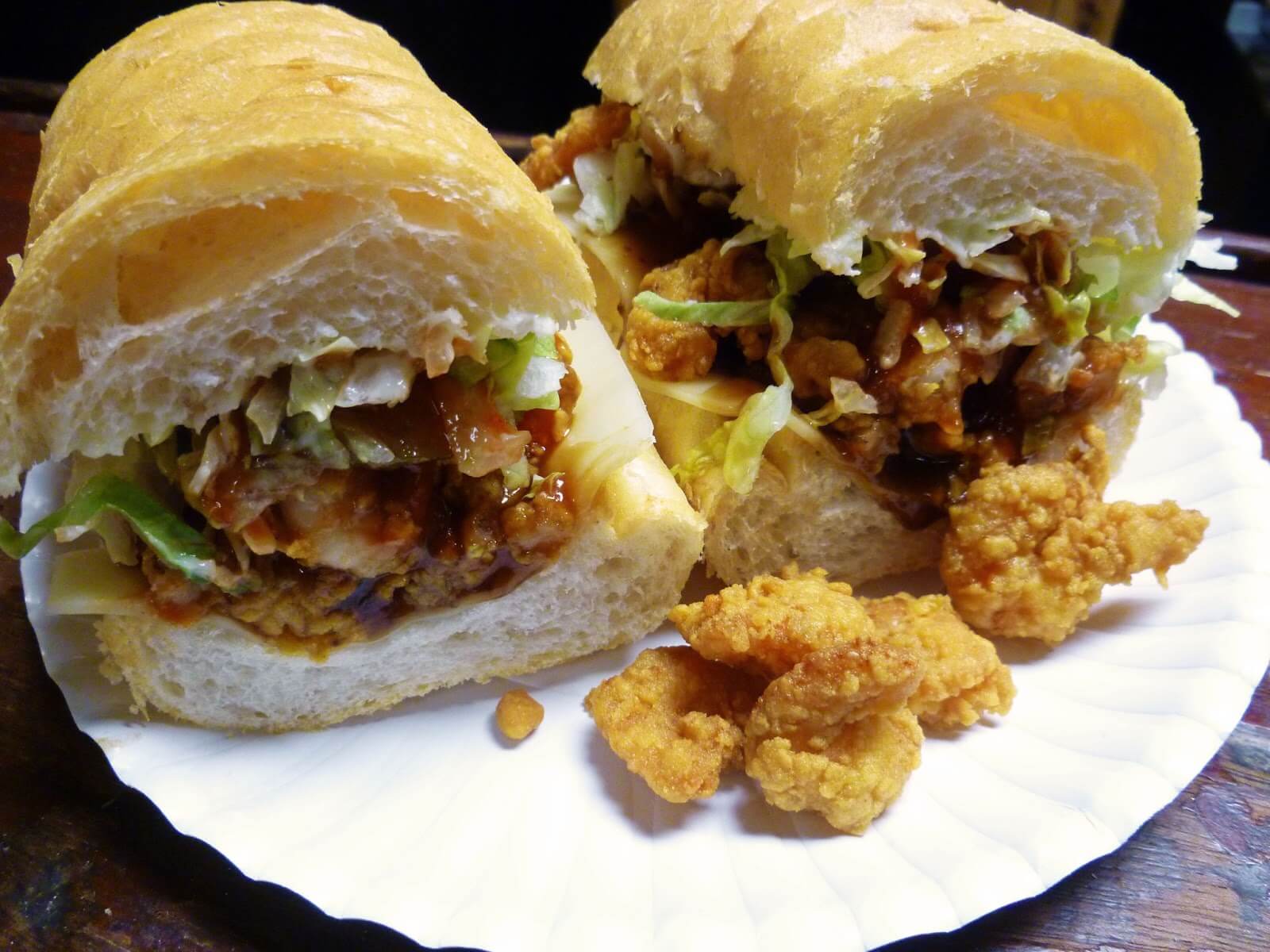 A fully dressed shrimp po'boy at Domilise's in New Orleans, crispy fried shrimp spilling from a toasted French roll with shredded lettuce on a paper plate.