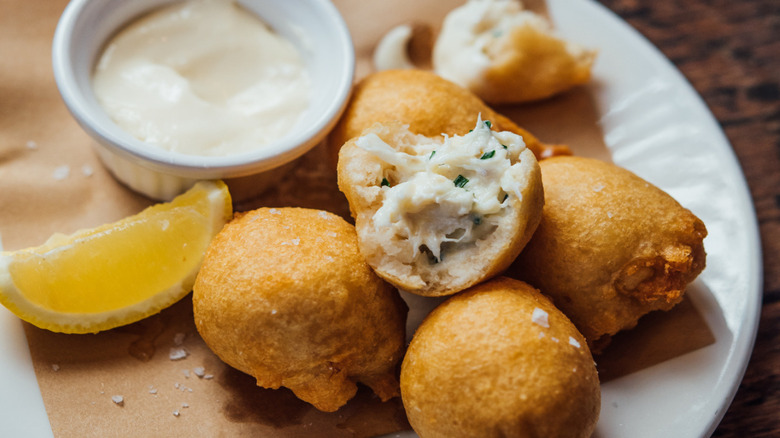 Golden crab beignets served with lemon and rémoulade at La Petite Grocery in New Orleans, crisp fritters on parchment over a white plate.