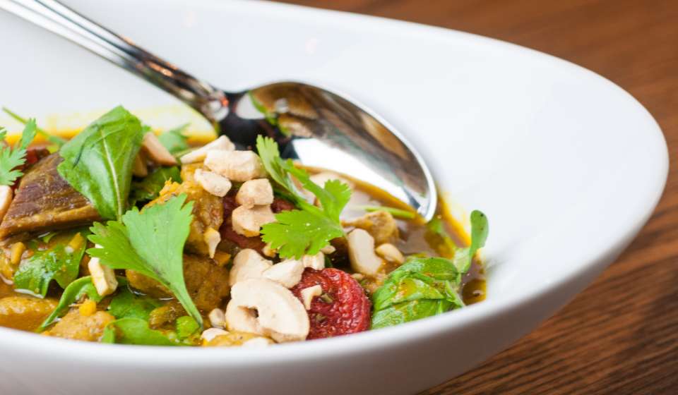 Curried goat with sweet potato gnocchi, roasted tomatoes, cashews and cilantro at Compère Lapin in New Orleans, served in a wide white bowl.