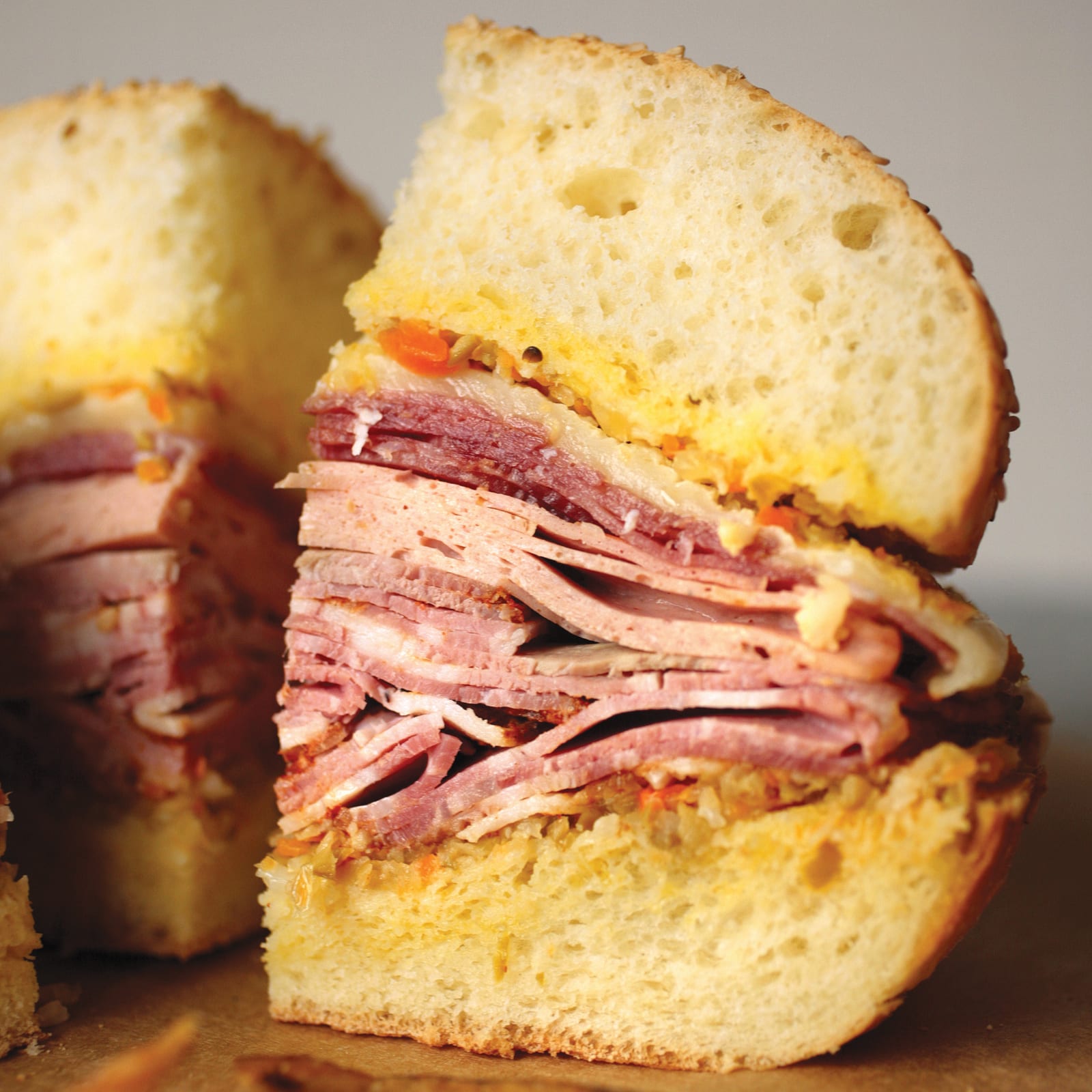 A cross-section of the muffuletta at Cochon Butcher in New Orleans, layers of cured meats, cheese and olive salad pressed in sesame-studded bread.
