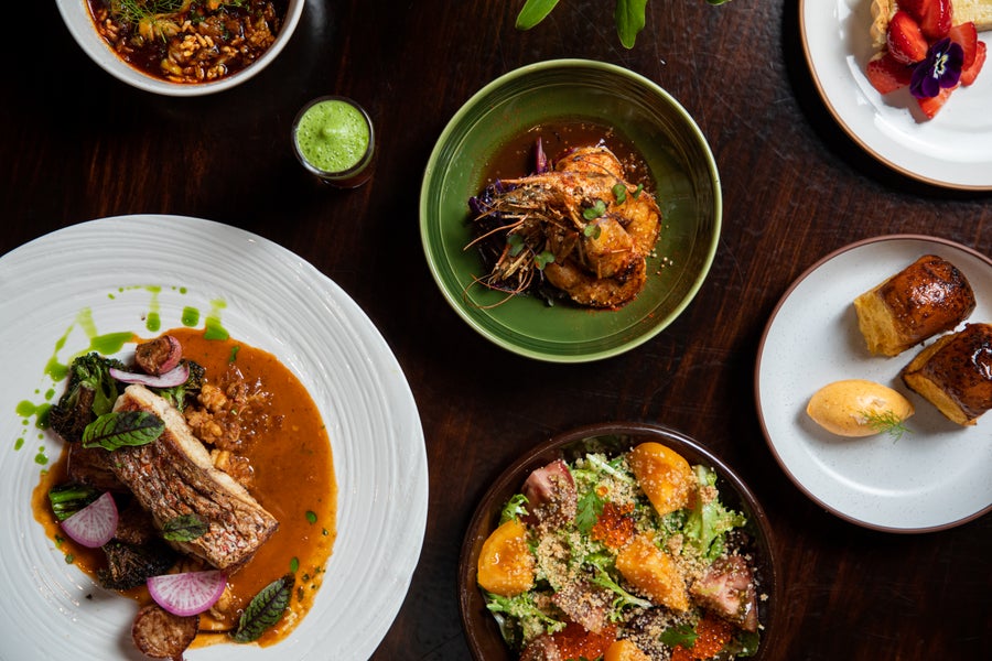 An overhead view of Dakar NOLA's Senegalese tasting menu in New Orleans — colorful small plates with seafood, grains and vibrant garnishes on white dishes.