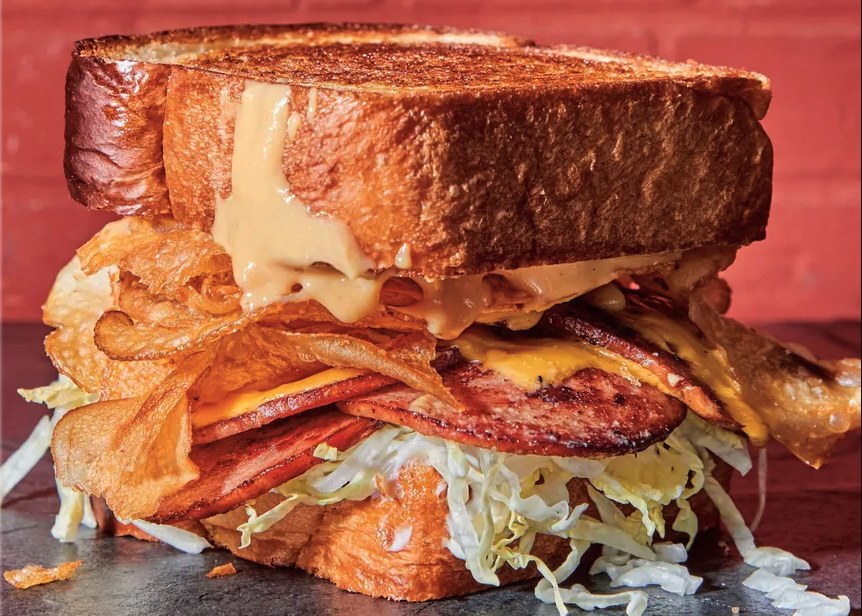 The fried bologna sandwich at Turkey and the Wolf in New Orleans — a thick stack of crispy bologna, slaw and chips on toasted bread with a branded flag.