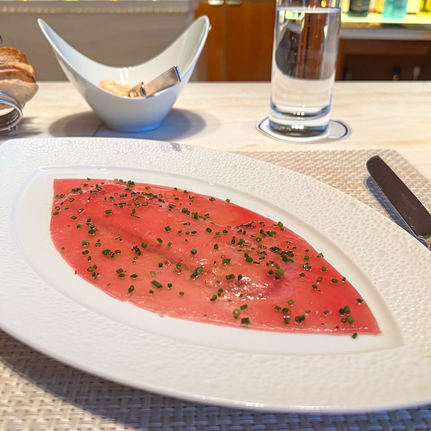 Le Bernardin's yellowfin tuna carpaccio, thinly pounded, with chives on a white plate