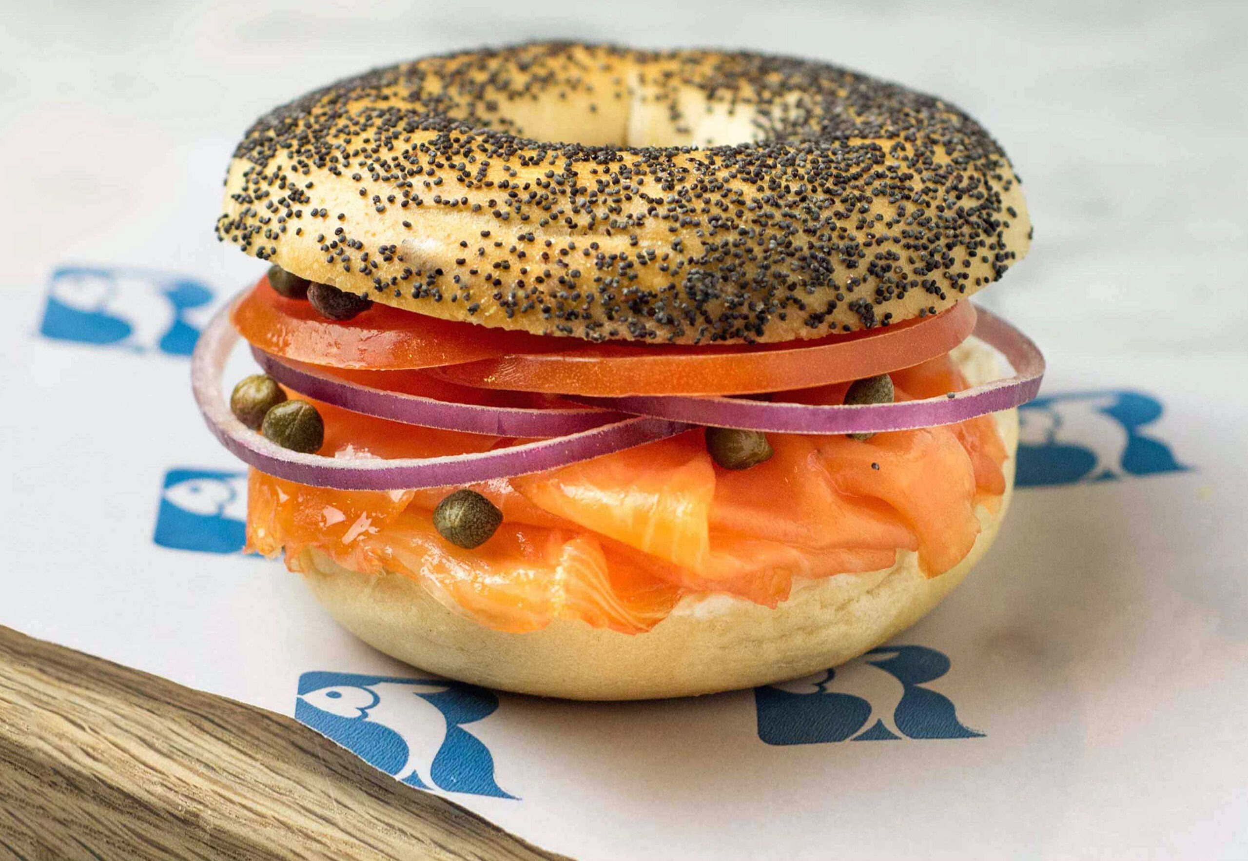 Hero: poppy bagel with lox, tomato, red onion, and capers on Russ & Daughters branded paper