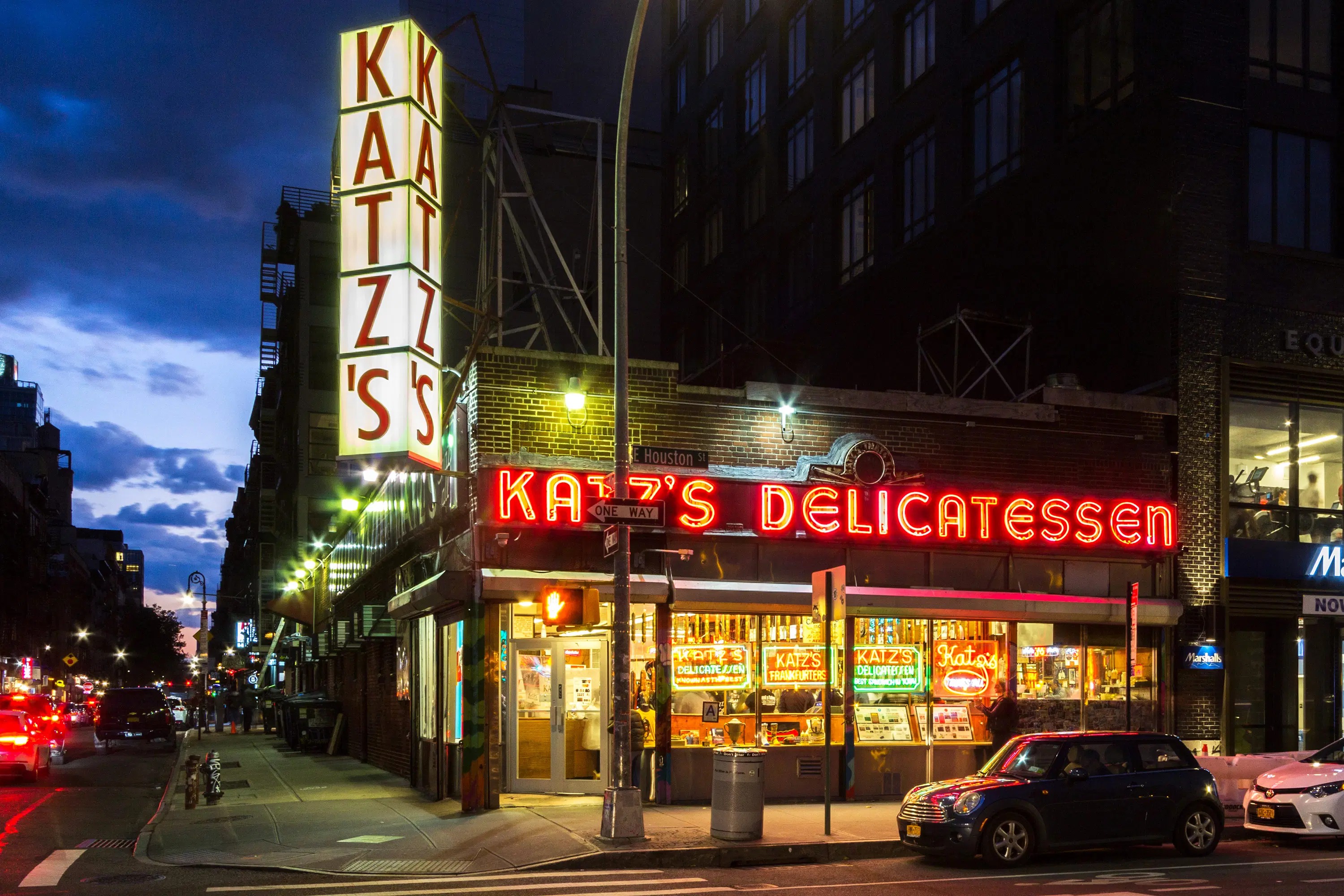 Katz's Delicatessen at dusk: the vertical KATZ'S sign and red neon Delicatessen marquee on E Houston St