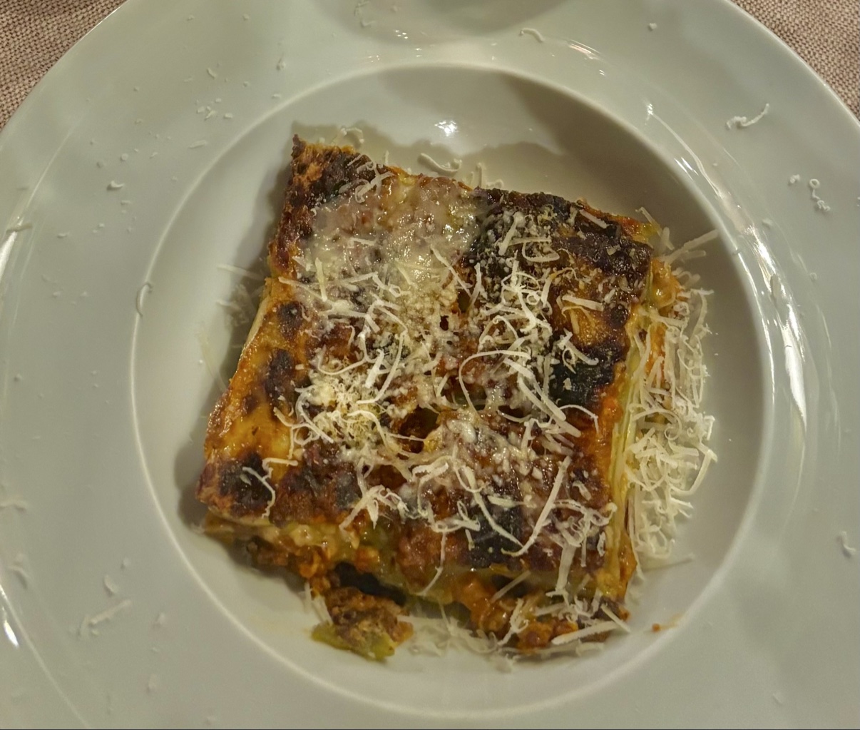 A square-cut slice of lasagna alla bolognese with a deeply browned, crisped cheese crust under a snowfall of Parmigiano-Reggiano at Al Sangiovese in Bologna.