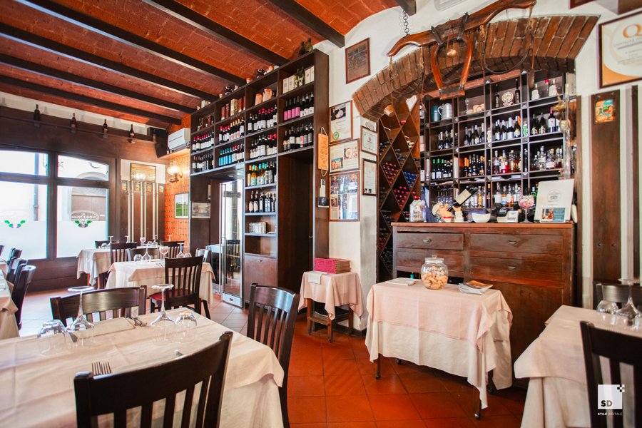 The dining room at Al Sangiovese in Bologna — wood-paneled walls, set tables, and the bottle-lined wine wall