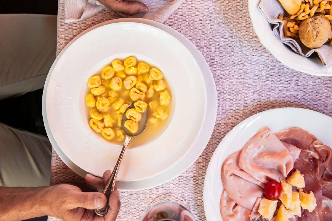 Tortellini in brodo at Al Sangiovese in Bologna — hand-folded tortellini in clear golden broth, served with prosciutto di Parma, mortadella, and Parmigiano-Reggiano