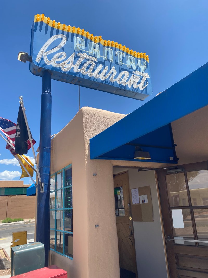 The Pantry Restaurant's vintage neon sign on its pole above Cerrillos Road in Santa Fe, New Mexico — cursive script outlined in yellow bulbs, beckoning diners since 1948