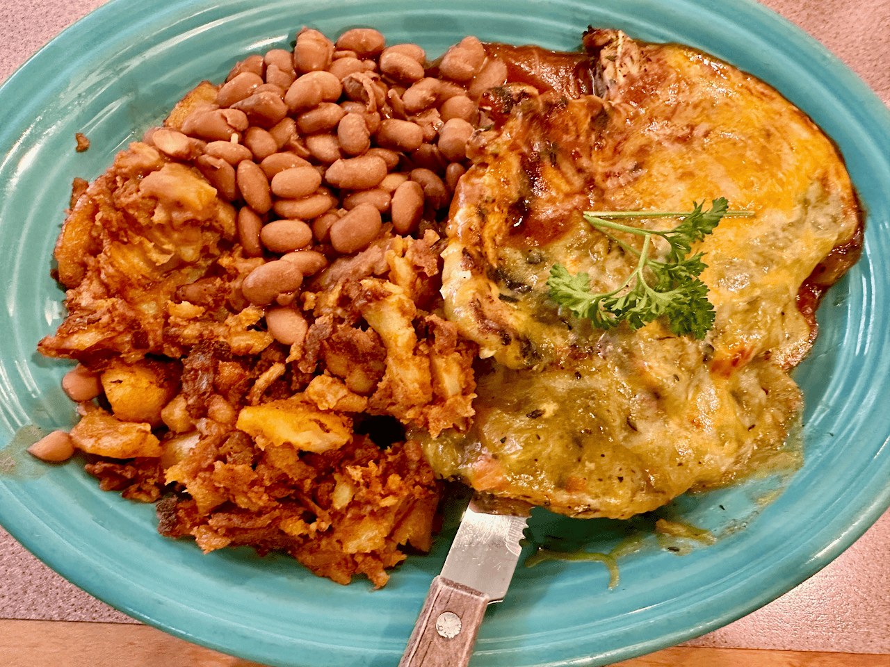 The Pantry's pork chop special in Santa Fe — a bone-in pork chop smothered in red and green chile under a blanket of melted cheese, with papas and pinto beans