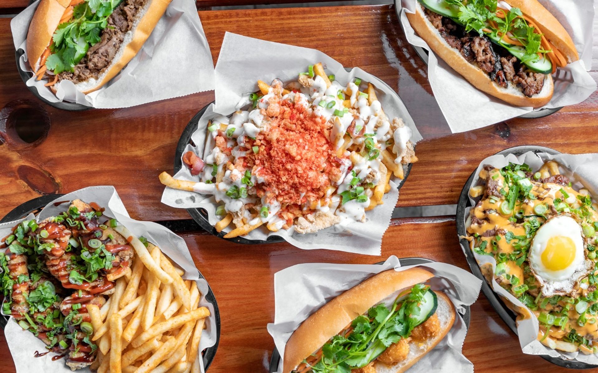 A spread at Banh Mi Boys: banh mi, loaded fries with a fried egg, and Korean fried chicken.