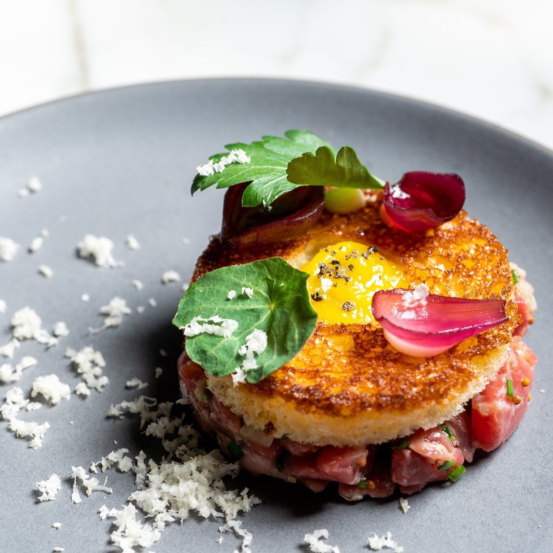 Sepia's steak tartare — hand-cut beef under a crisp beef-fat toast slab with nasturtium, pickled red onion, aioli, and grated cheese.
