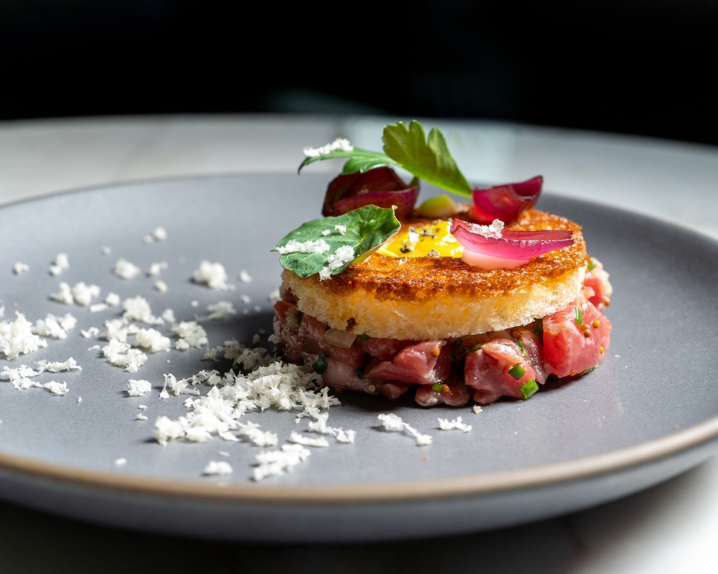 A side view of Sepia's steak tartare showing the crisp beef-fat toast slab over hand-cut beef with chives and grated cheese.